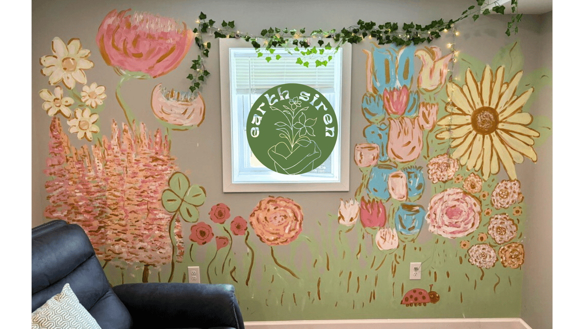 Wall mural of colorful oversized flowers painted by Elizabeth Schirk for The Earth Siren. Features textured florals in pink, gold, and green surrounding a window, bringing nature indoors